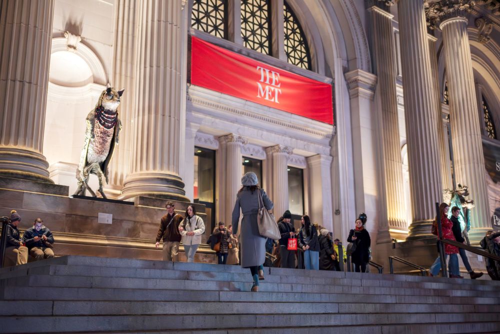 Visitors walking outside the illuminated entrance of the Metropolitan Museum of Art at night in New York City.