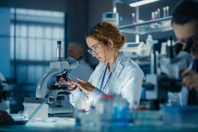 Hisplanic Female Bioengineer Looking at DNA Samples Under a Microscope in a Modern Applied Science Laboratory. Portrait of a Young Lab Engineer in White Coat Inventing New Medical Drugs