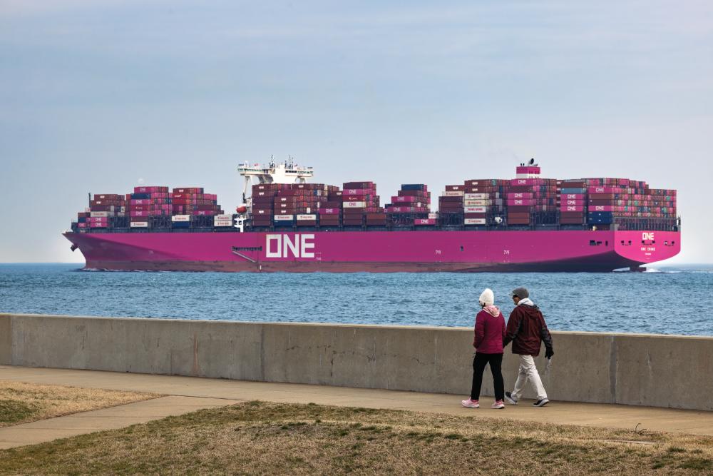 People walk along a trail as a container ship enters the Chesapeake Bay in Fort Monroe.