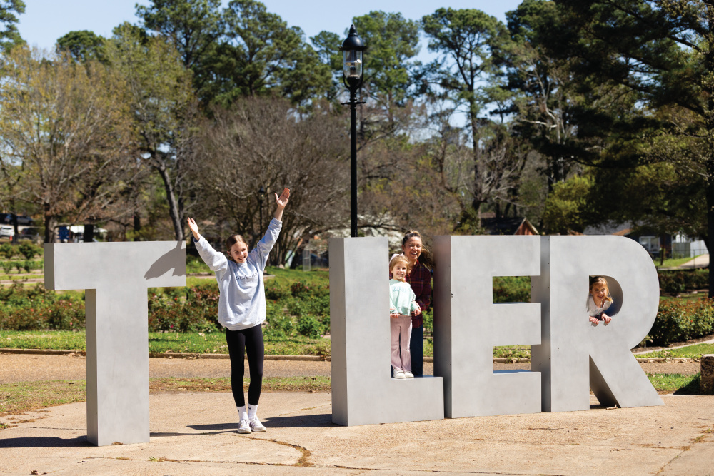 A family takes photos with a Tyler sign at Tyler Rose Garden in Tyler, Texas.