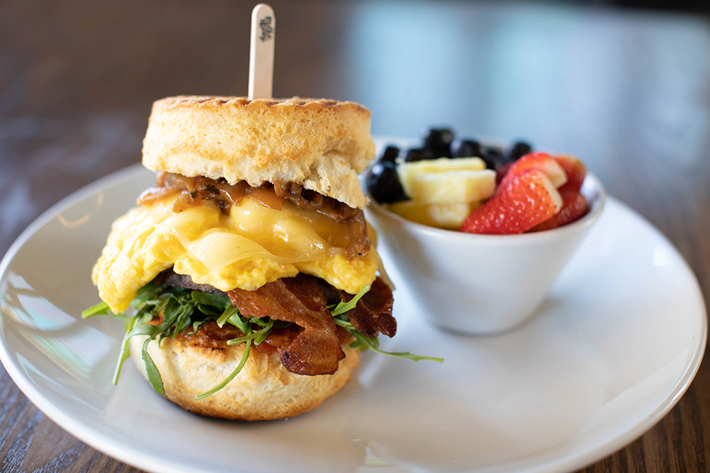 The Farmhouse Biscuit from Milk & Honey at Market South in Chattanooga, TN, is made with breakfast sausage, Applewood bacon, buttermilk biscuit, tomato jam, scrambled egg, arugula, white cheddar and caramelized onion and is served with a side of fresh fruit.