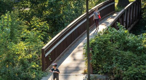 Visitors cross a bridge across Ioway Creek at Brookside Park in Ames, Iowa.