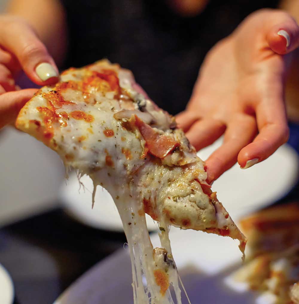 Woman is pulling slice of pizza from plate