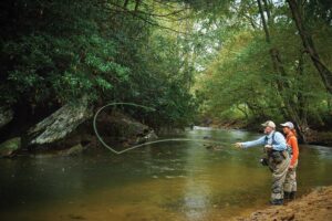 Men standing in knee-deep river water casting a fly fishing rod.