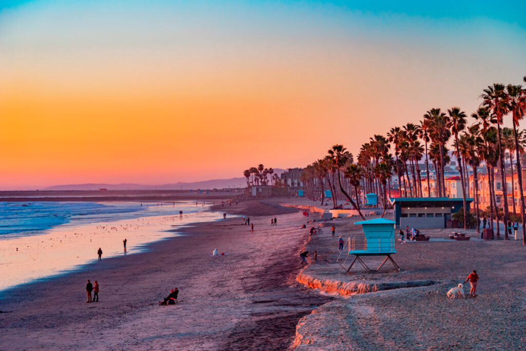 People walking and relaxing along a sandy beach in Oceanside California near Carlsbad at sunset.