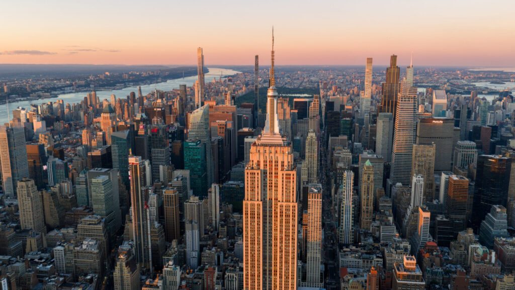 New York, United States, on September 21, 2025 Aerial view of the Empire State Building illuminated by sunset light above Midtown skyscrapers with Central Park and the Hudson River visible in the distance Camera position elevated high angle facing north over Manhattan