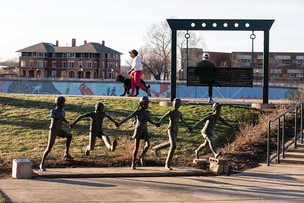 bronze statue standing along a brick walkway in a green park near downtown Dayton.