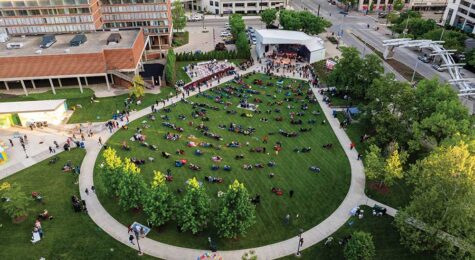 Large outdoor crowd sitting on lawn chairs in front of a brightly lit concert stage at night.