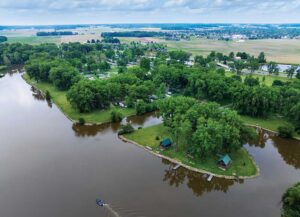 Aerial view of motorboats cruising across a large blue lake surrounded by green trees and fields.