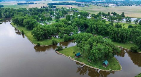 Aerial view of motorboats cruising across a large blue lake surrounded by green trees and fields.