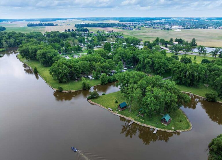 Aerial view of motorboats cruising across a large blue lake surrounded by green trees and fields.