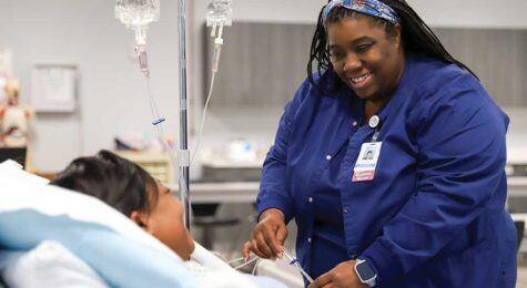 A student wearing scrubs practicing clinical procedures on a medical mannequin in a simulation lab.