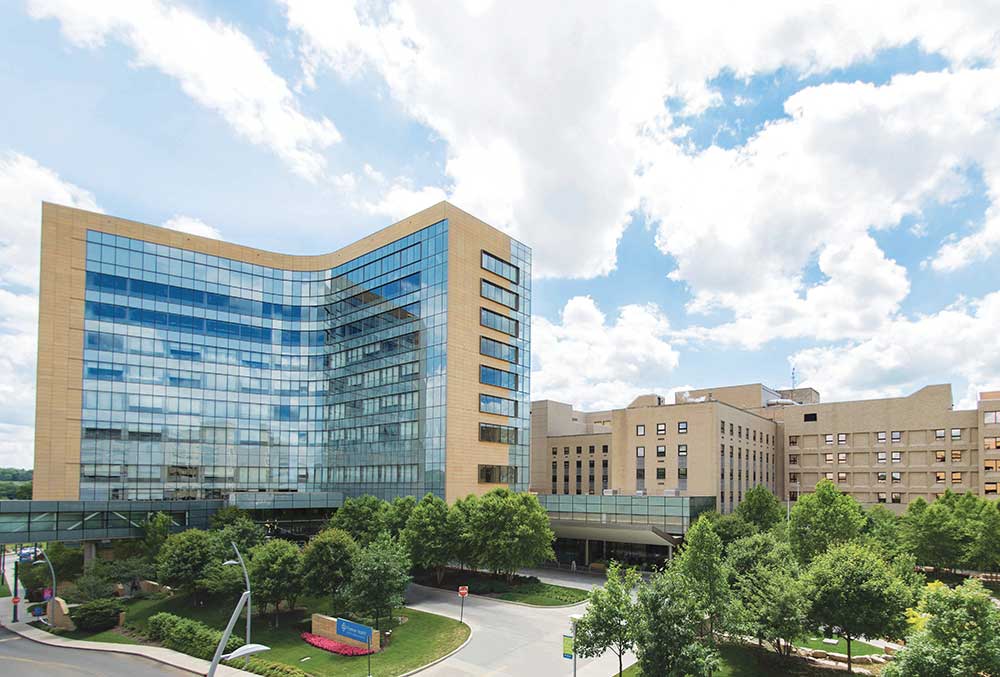 Exterior shot of the glass and stone facade of Premier Health's Miami Valley Hospital building surrounded by green trees.