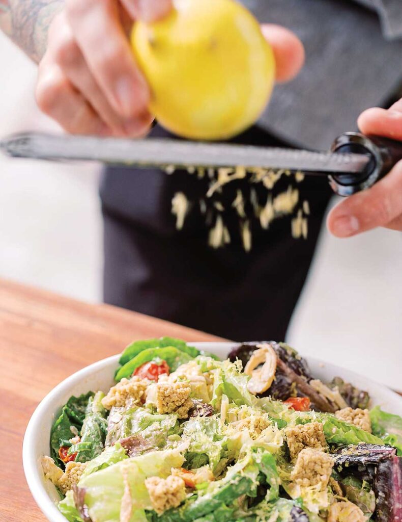 Chef zesting lemon over a leafy green salad with croutons and tomatoes at Herban Market in Franklin, Tennessee