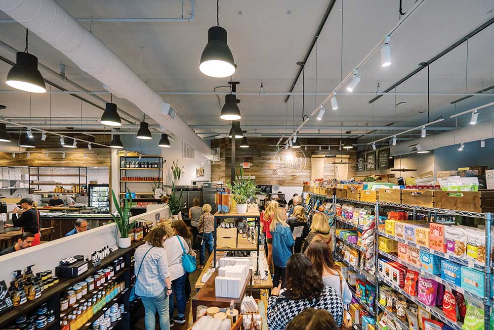 Shoppers walking through the bright, plant-filled aisles of Herban Market organic grocery in Franklin, Tennessee.