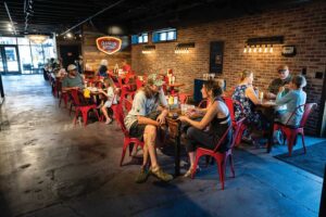 Customers eating at tables with red metal chairs inside The Franklin Butchery’s brick-walled dining room