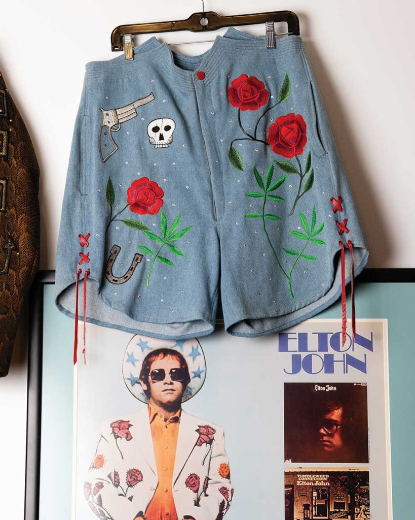 Silver suit jacket embroidered with red, blue and purple roses on a hanger, designed by Manuel