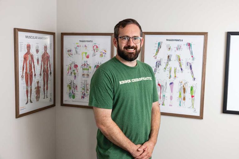 Franklin TN chiropractor Dr. Bradley Krock smiling in a green Krock Chiropractic T-shirt in front of framed anatomy charts