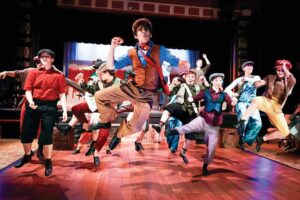 Teen actors in newsboy caps and vests jumping mid-dance during a musical at the Williamson County Performing Arts Center in Franklin, TN