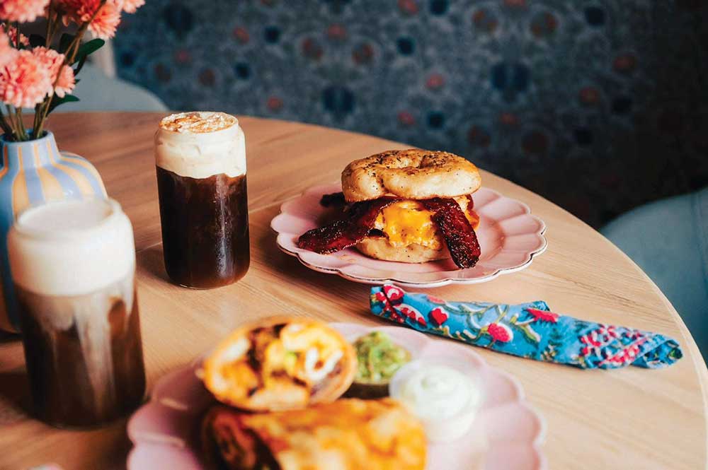 Iced cold brew with cream next to a bacon, egg and cheese sandwich and a breakfast burrito on pink plates at The Brunch Collective in Spring Hill, TN