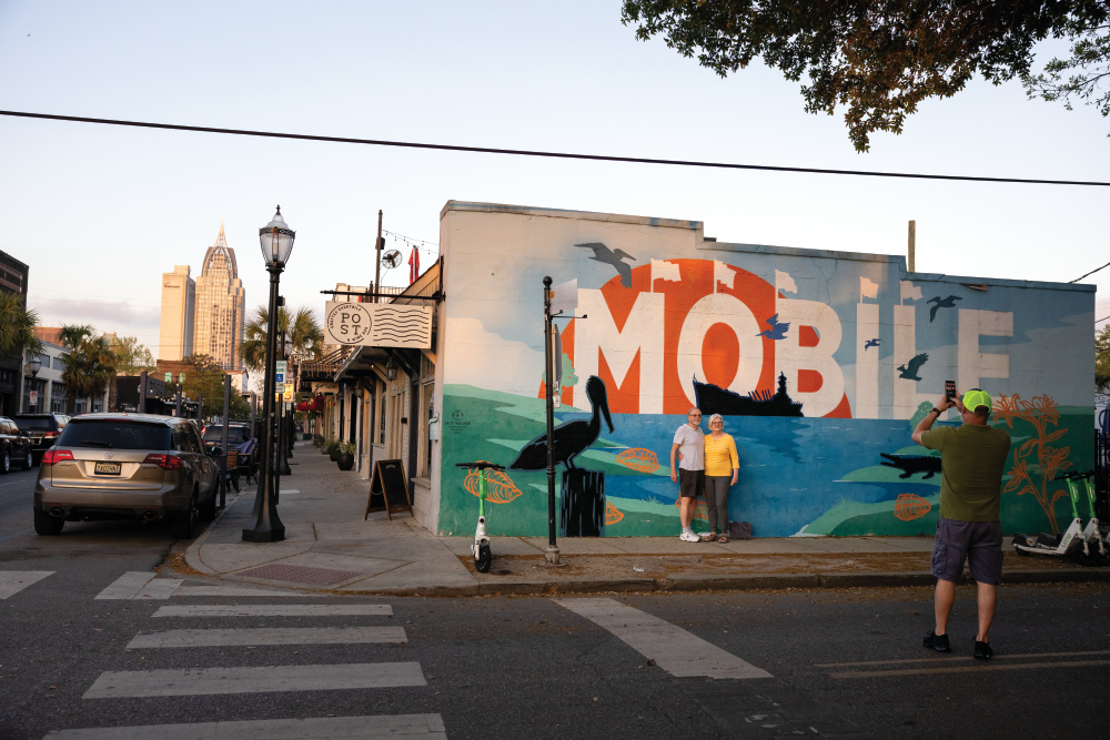 People take a photo with a mural in downtown Mobile.