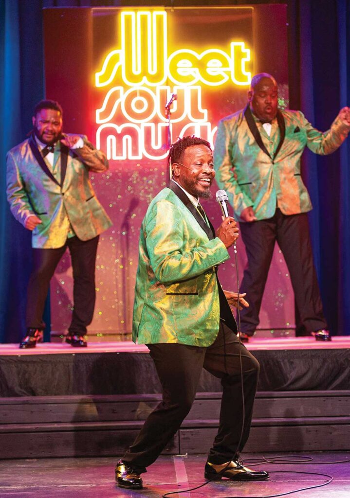 Three singers in sparkly green and gold jackets performing under a neon “Sweet Soul Music” sign on a Franklin, Tennessee, stage
