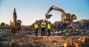 Construction Site With Excavators on Sunny Day: Diverse Team Of Male And Female Specialists Discussing Real Estate Project. Civil Engineer, Architect And Investor Talking About Apartment Building.