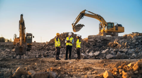 Construction Site With Excavators on Sunny Day: Diverse Team Of Male And Female Specialists Discussing Real Estate Project. Civil Engineer, Architect And Investor Talking About Apartment Building.